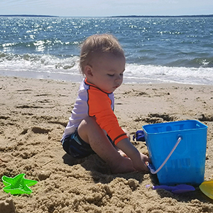 Young baby at the beach playing with a bucket of sand and beach toys