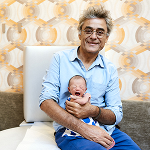 Doctor Michel Cohen of Tribeca Pediatrics holding newborn baby and smiling while sitting on exam table in Tribeca Pediatrics office