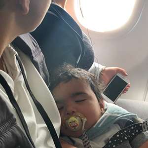 Young baby with a pacifier sleeping on parent's arms on a plane