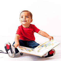 Young boy smiling and wearing a bright red t-shirt holding a picture book open