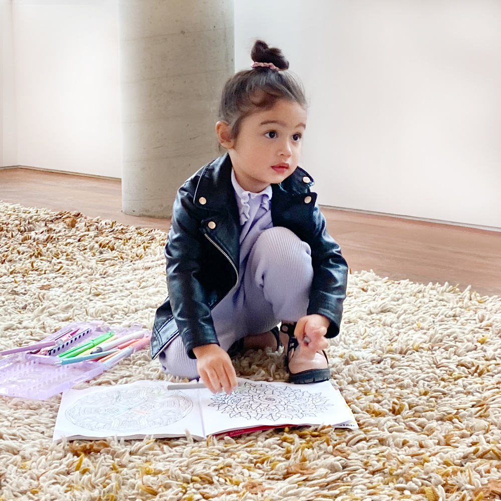 Young girl sitting on a carpet on the floor playing with a coloring book